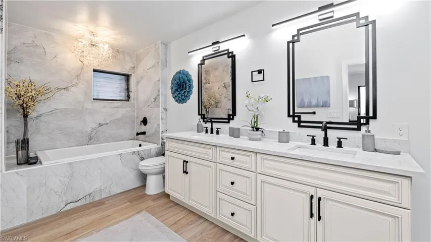 Full bath featuring double vanity, light wood-type flooring, a combined bath / shower with marble appearance, and a chandelier