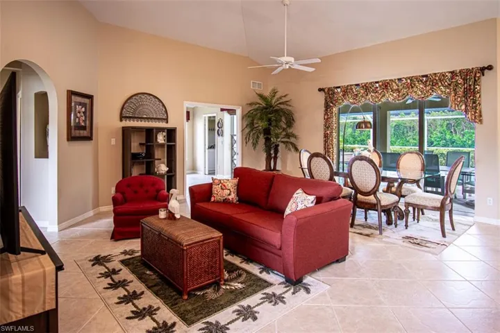 Living area featuring light tile patterned floors, arched walkways, ceiling fan, and high vaulted ceiling