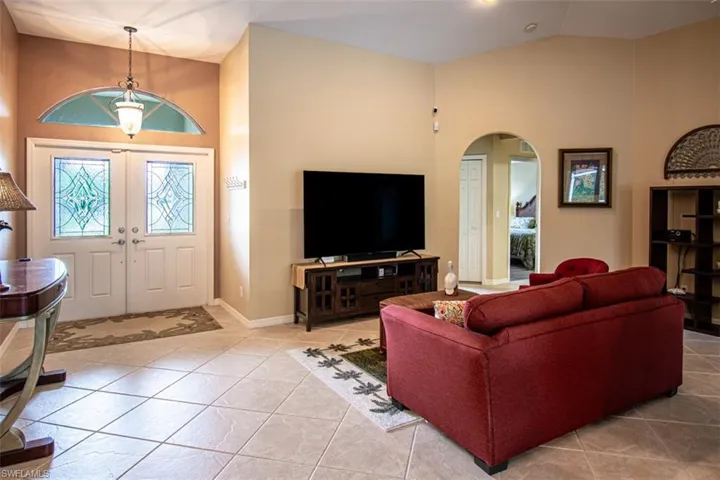 Living room with high vaulted ceiling, tile patterned flooring, and arched walkways