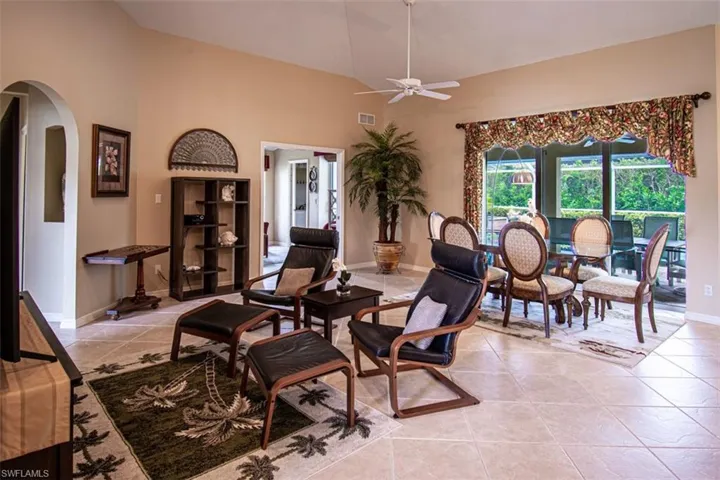 Living room with lofted ceiling, arched walkways, light tile patterned flooring, and ceiling fan
