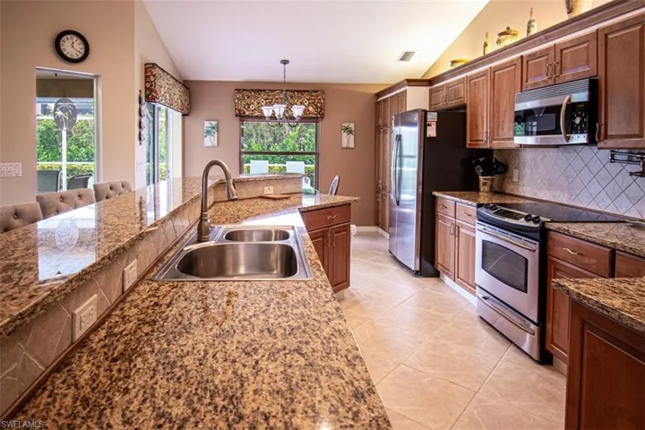 Kitchen with vaulted ceiling, stainless steel appliances, light tile patterned floors, decorative backsplash, and hanging light fixtures