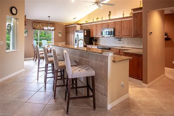 Kitchen with light stone countertops, brown cabinets, a breakfast bar, vaulted ceiling, and a kitchen island with sink