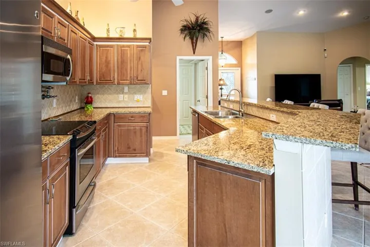 Kitchen featuring appliances with stainless steel finishes, brown cabinets, a kitchen island with sink, arched walkways, and hanging light fixtures