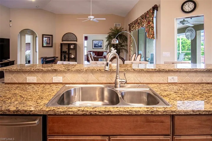 Kitchen featuring a ceiling fan, open floor plan, light stone counters, brown cabinetry, and vaulted ceiling