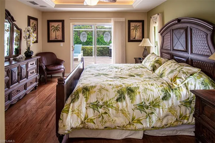 Bedroom with access to exterior, dark wood-type flooring, a tray ceiling, a ceiling fan, and crown molding