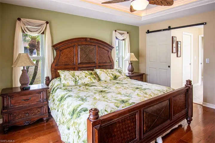 Bedroom with a barn door, ornamental molding, dark wood finished floors, a ceiling fan, and a raised ceiling