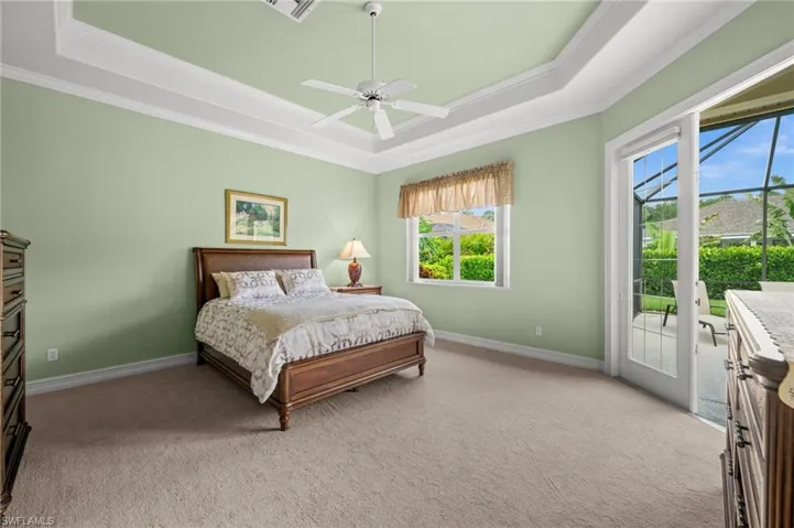 The spacious primary suite offers a peaceful retreat with tray ceilings, new carpet, abundant natural light, and direct access to the outdoor living areas.