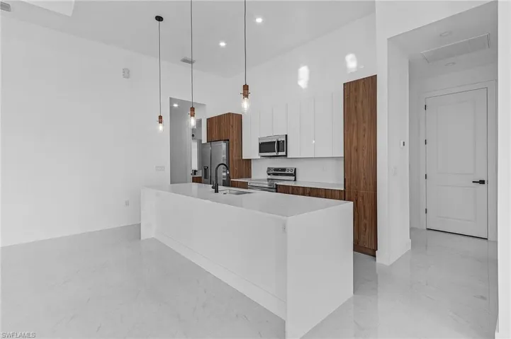 Kitchen featuring a kitchen island with sink, sink, hanging light fixtures, white cabinetry, and stainless steel appliances