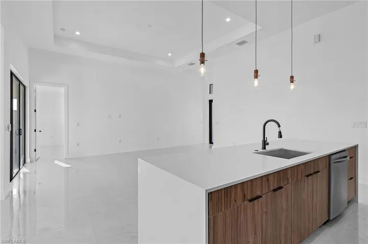 Kitchen with decorative light fixtures, sink, a kitchen island with sink, and a tray ceiling