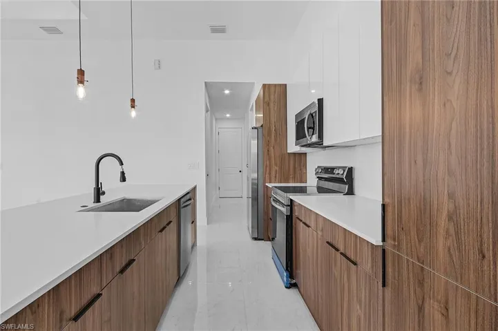 Kitchen with white cabinets, appliances with stainless steel finishes, decorative light fixtures, and sink