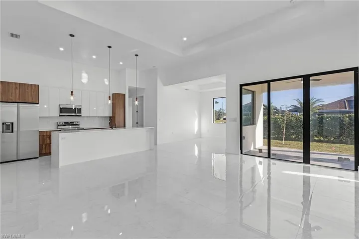 Kitchen featuring stainless steel appliances, a tray ceiling, a kitchen island with sink, pendant lighting, and white cabinets