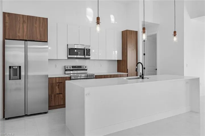 Kitchen featuring a kitchen island with sink, sink, hanging light fixtures, appliances with stainless steel finishes, and white cabinetry