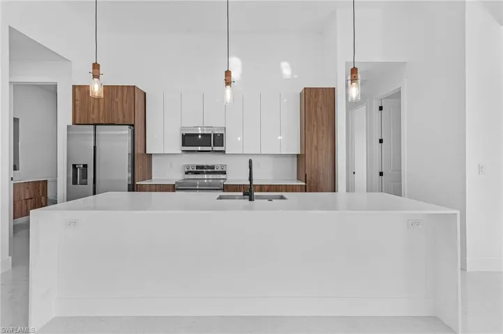 Kitchen featuring stainless steel appliances, a kitchen island with sink, sink, pendant lighting, and white cabinetry