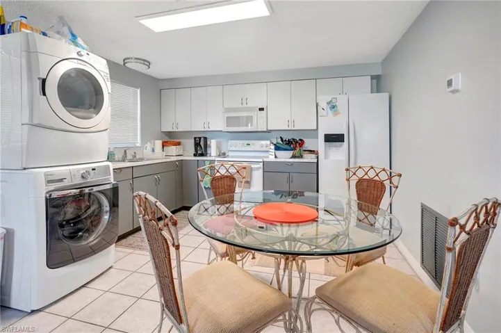 Washroom with stacked washer and clothes dryer, sink, and light tile floors