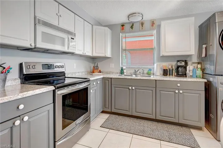 Kitchen with gray cabinets, stacked washer / drying machine, stainless steel electric range oven, sink, and light tile floors