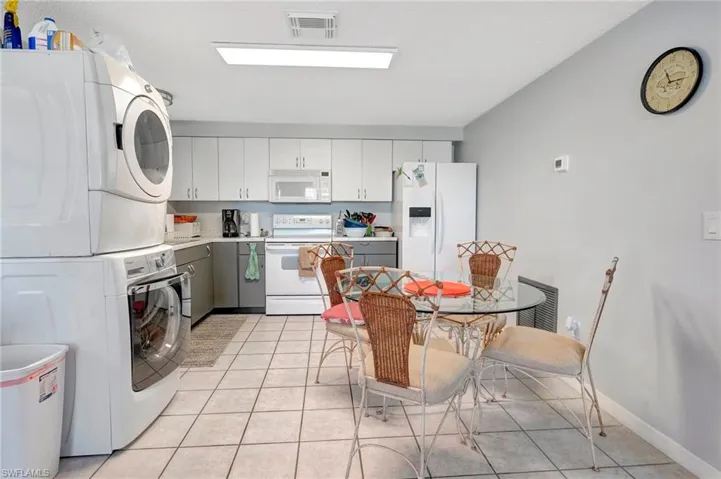 Kitchen with light tile floors, white cabinets, white appliances, and stacked washer / drying machine