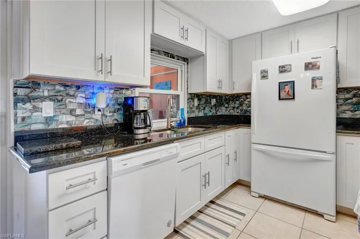 Kitchen with tasteful backsplash, white cabinetry, dark stone countertops, sink, and white appliances