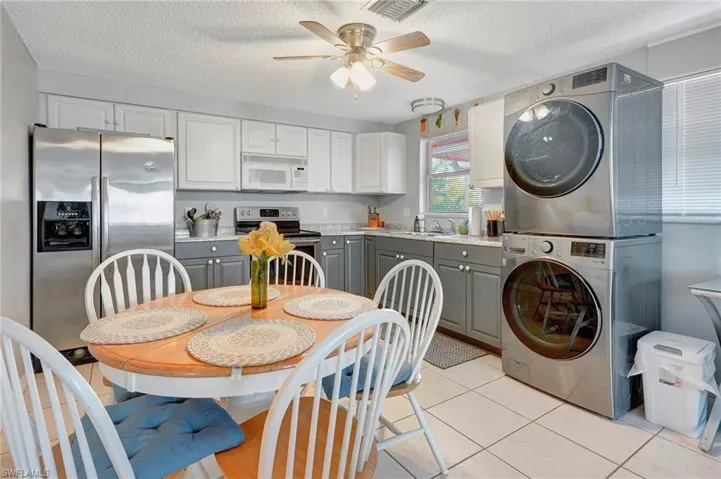 Clothes washing area featuring ceiling fan, stacked washer and clothes dryer, a textured ceiling, light tile floors, and sink
