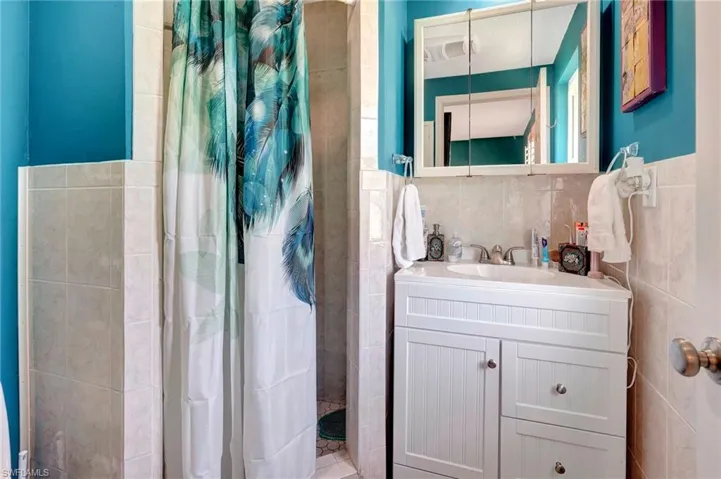 Bathroom with tasteful backsplash, tiled shower, vanity, and tile walls