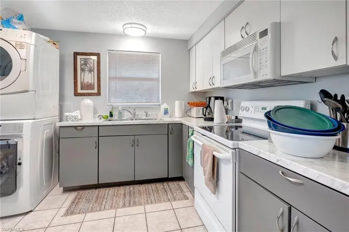 Kitchen featuring gray cabinetry, white appliances, stacked washing maching and dryer, sink, and light tile floors