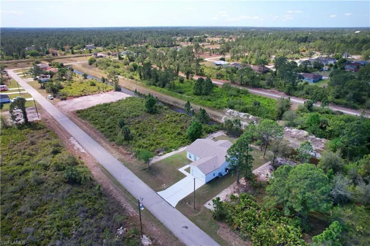 The property features a private driveway and a light-colored exterior, surrounded by natural landscaping and trees