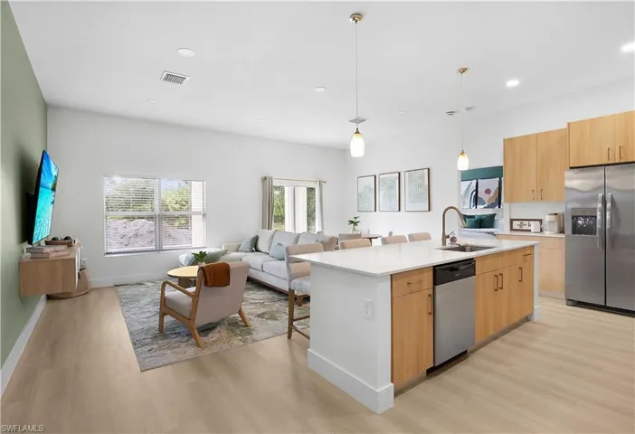 Open-concept living area featuring light wood flooring, a kitchen island with a white countertop and integrated sink, stainless steel appliances, and recessed lighting