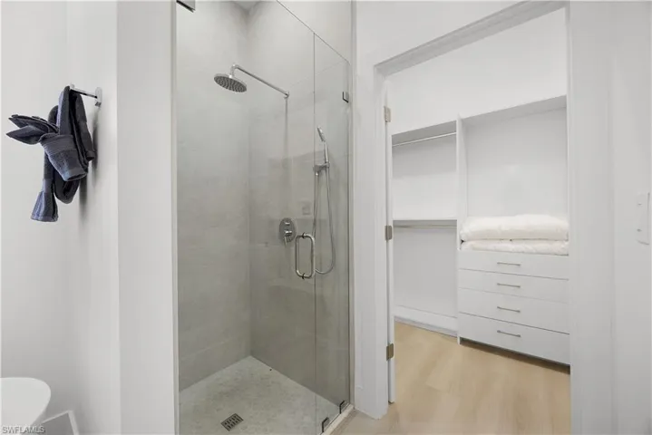 The bathroom features a glass-enclosed shower with a rainfall showerhead and a separate handheld shower, complemented by a well-organized closet with shelving and drawers