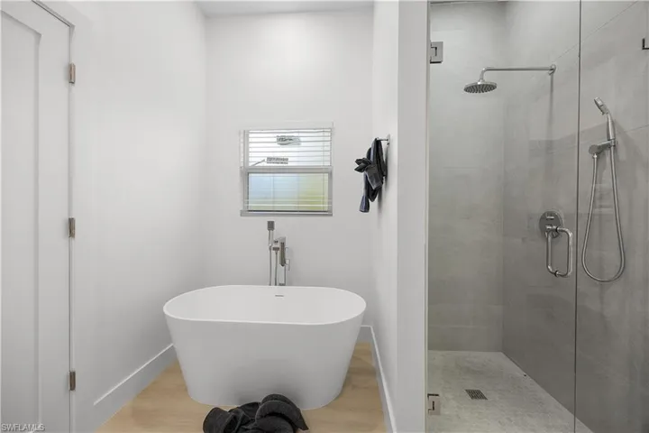 This bathroom features a freestanding soaking tub with a floor-mounted faucet, a glass-enclosed shower with a rain shower head and hand-held shower, and light-colored flooring