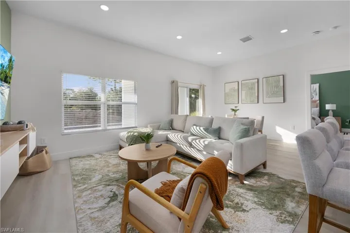 Living area with light wood-style flooring, a large window with blinds, and recessed lighting