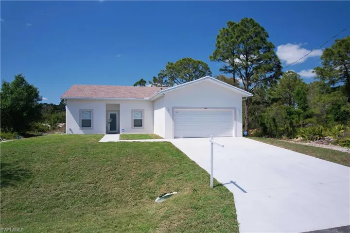 The property features a white exterior, a well-maintained lawn, and a spacious concrete driveway leading to an integrated garage