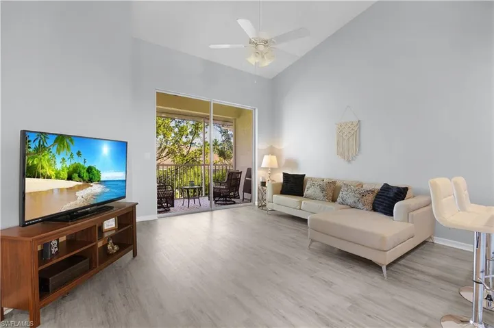 The living area features light-toned flooring, a vaulted ceiling, and sliding glass doors that open to an outdoor balcony