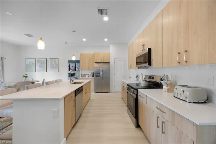 The kitchen features light-toned cabinetry, stainless steel appliances, and sleek white countertops