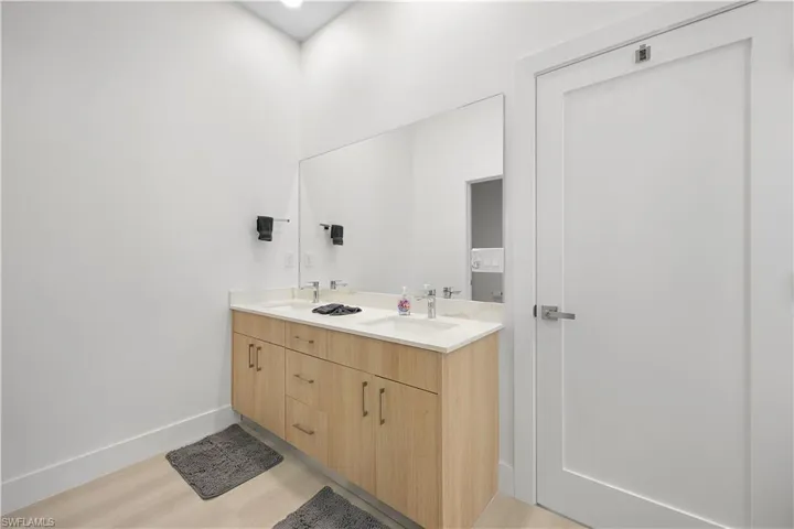 Bathroom vanity featuring dual sinks, a large mirror, and light wood cabinetry with brushed nickel hardware