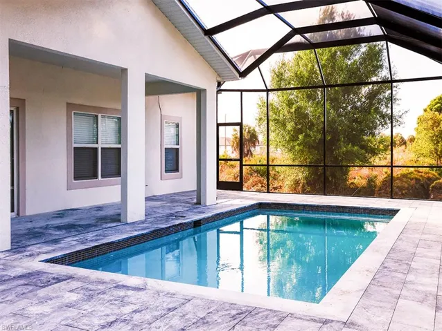 The property features a screened-in swimming pool area with a tiled surround, an outdoor living space with a covered patio, and large windows with blinds
