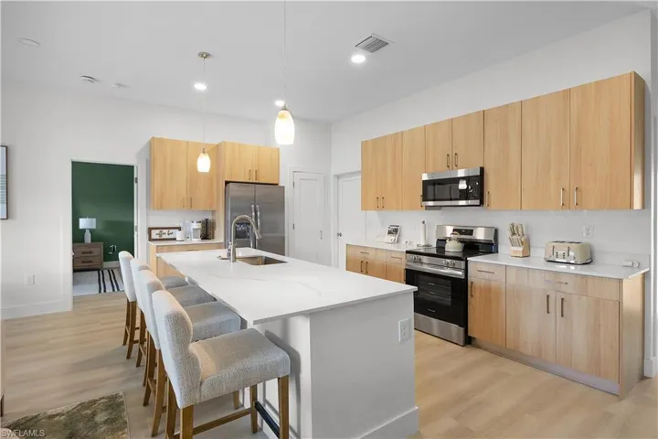 The kitchen features light wood cabinetry, stainless steel appliances, and an island with a white countertop and seating for four