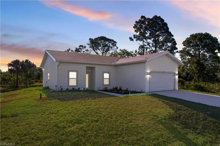 The property features a well-maintained lawn, a paved driveway, and an attached garage with exterior lighting fixtures