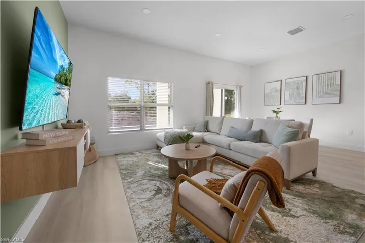 This living area features light-toned flooring, recessed lighting, and windows with blinds