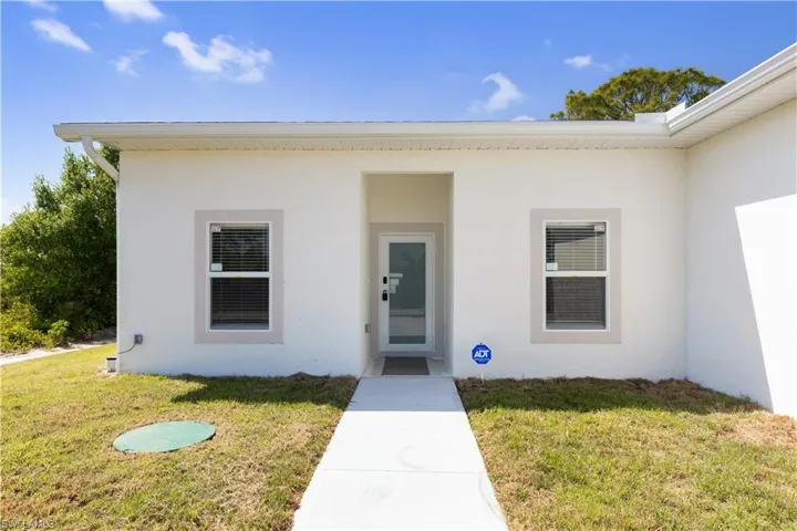The property features a white exterior with a light-colored trim around the windows and main entry, a white front door, and a concrete pathway leading to the entrance
