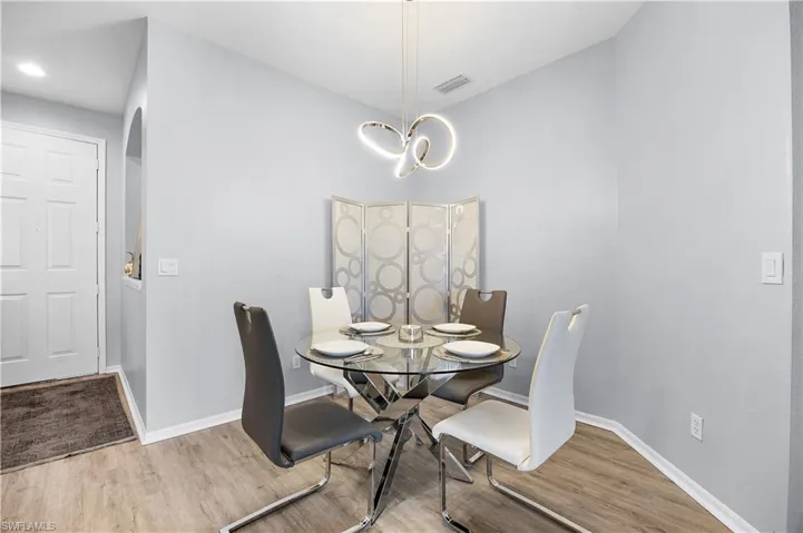 Dining area featuring a modern glass top table, a unique pendant light fixture, and wood-look flooring