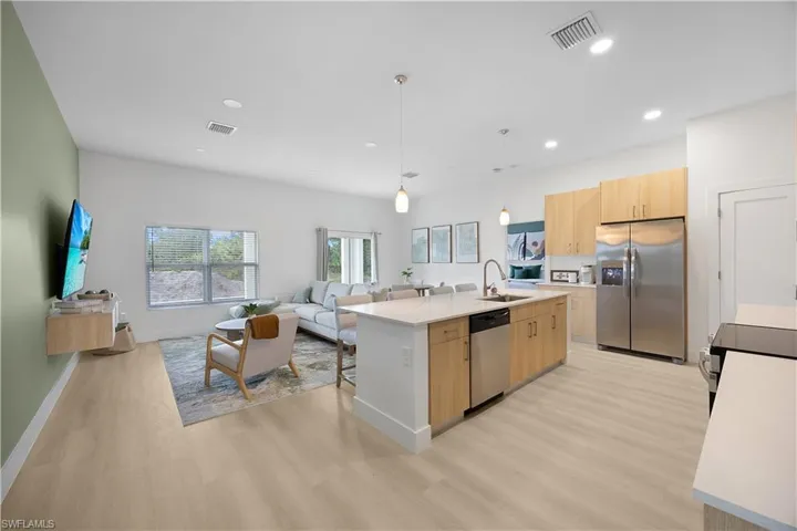 Open-concept living area with light-toned flooring, a kitchen island with a sink and dishwasher, light wood cabinetry, and stainless steel appliances