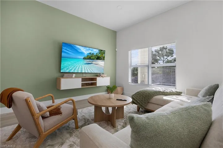 Living space featuring a wall-mounted television, a large window with horizontal blinds, and light-colored flooring