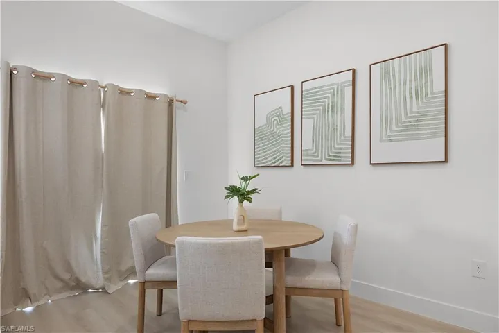Dining area featuring light-colored flooring, neutral-toned curtains, and a light wood-toned table with four upholstered chairs