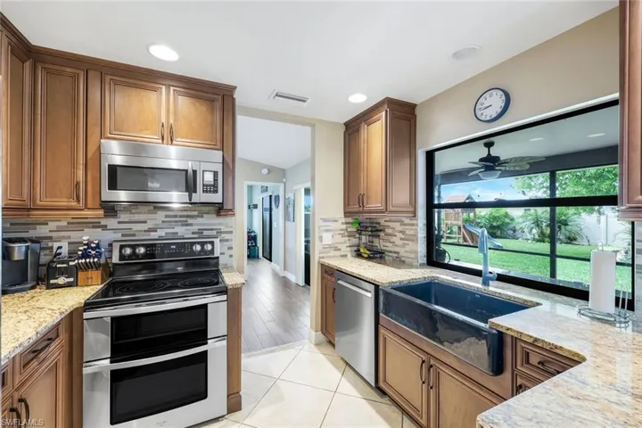 Kitchen with stainless steel appliances, light stone counters, tasteful backsplash, brown cabinetry, and recessed lighting