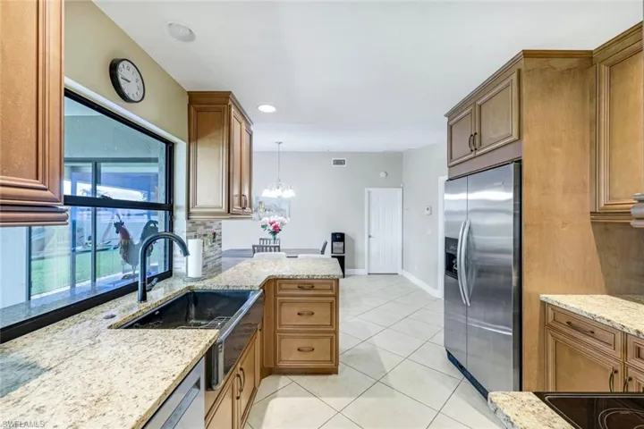 Kitchen with appliances with stainless steel finishes, a chandelier, light stone countertops, light tile patterned floors, and pendant lighting