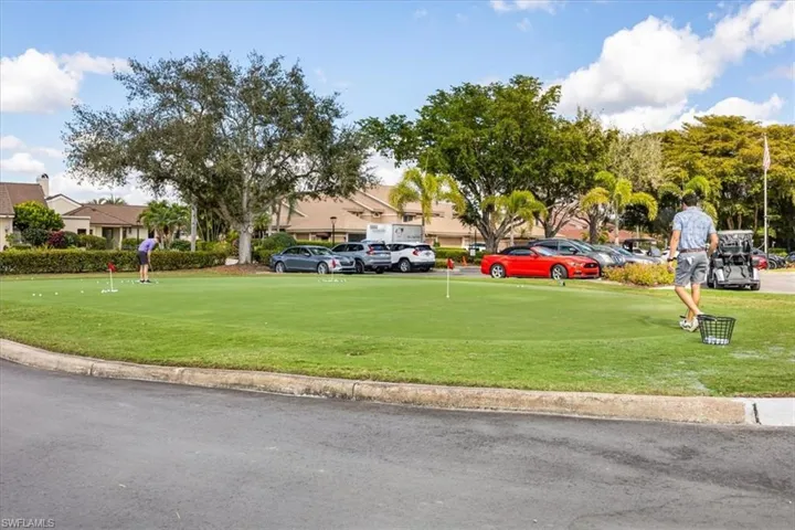 View of community with uncovered parking, a putting green, a lawn, and view of golf course