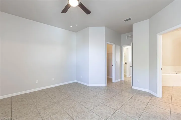 Unfurnished bedroom featuring a spacious closet, a ceiling fan, light tile patterned flooring, and ensuite bathroom