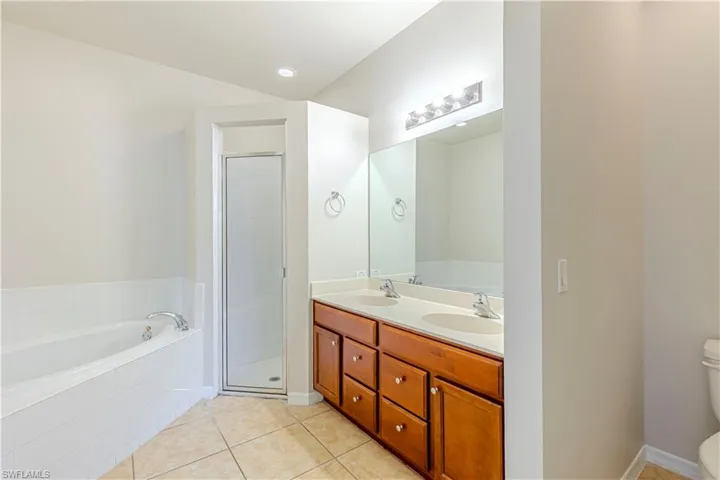Full bath featuring a bath, double vanity, light tile patterned floors, and a stall shower