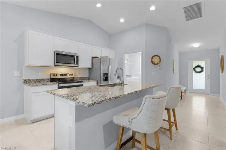 Kitchen featuring light stone counters, a center island with sink, visible vents, appliances with stainless steel finishes, and a sink