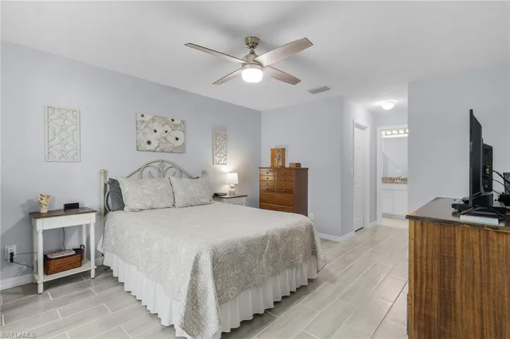 Bedroom featuring ceiling fan, ensuite bathroom, tile floors, visible vents, and baseboards