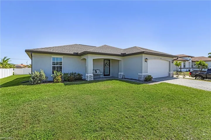 View of front of home with decorative driveway, stucco siding, fence, a garage, and a front lawn